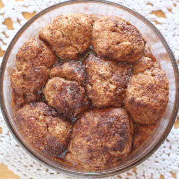 Baked balls of dough covered with cinnamon sugar in a clear baking dish.