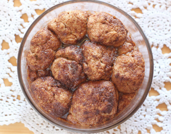 Baked balls of dough covered with cinnamon sugar in a clear baking dish.