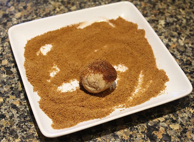 Ball of dough being rolled in a plate of cinnamon sugar.