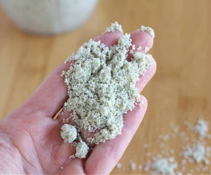 Green flour in a woman's hand with wood countertop in the background.