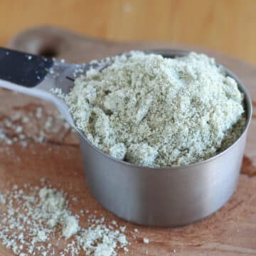 Light green flour in a measuring cup on a wooden cutting board.