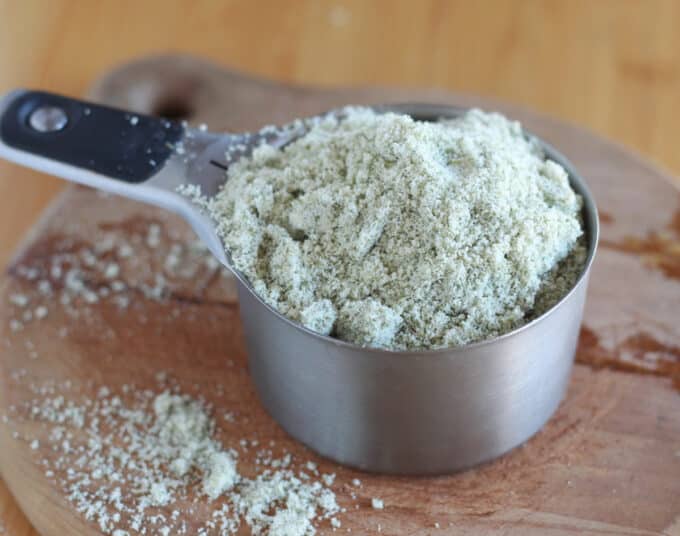 Light green flour in a measuring cup on a wooden cutting board.