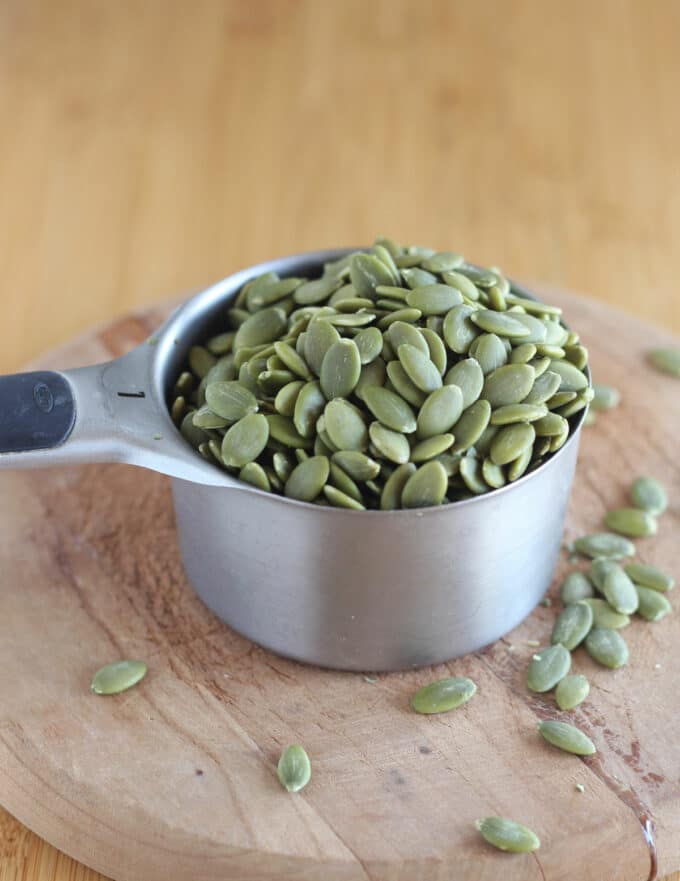 Measuring cup filled with green pumpkin seeds on a wood counter.