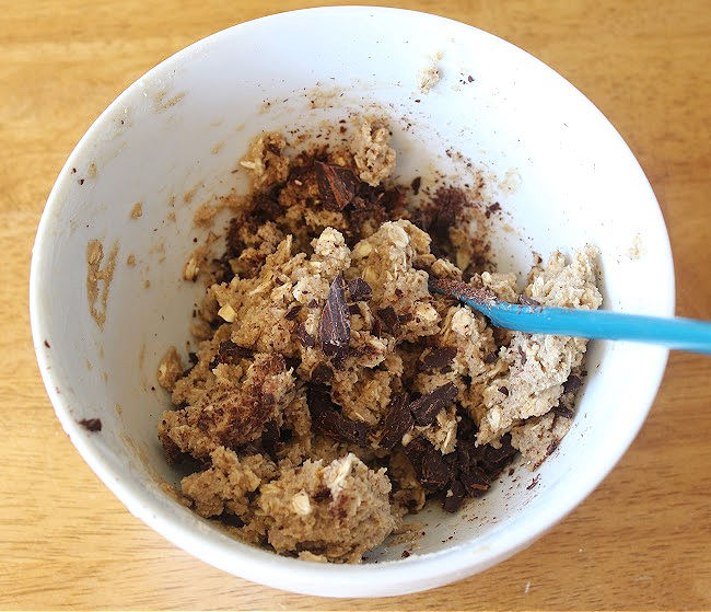 Dough mixed with chocolate chips in a bowl on a wood counter.