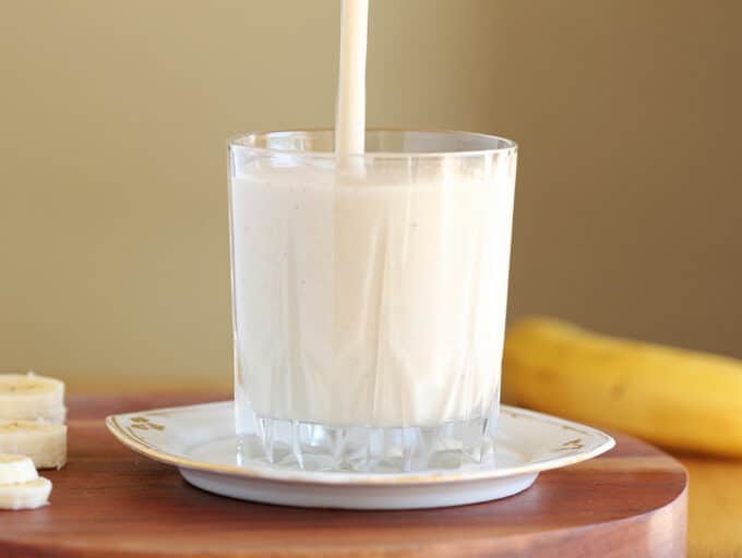 Smoothie being poured into a glass on a white plate.