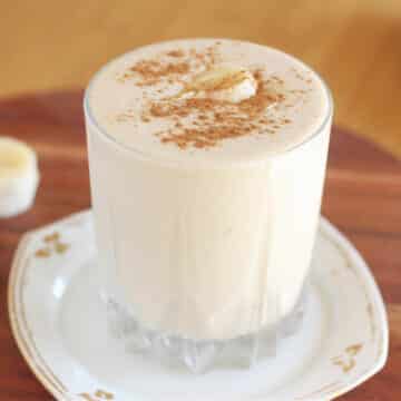 Smoothie in a glass topped with cinnamon and a banana slice.