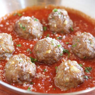 Multiple meatballs in marinara sauce in a steel pan.