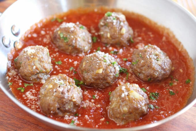 Multiple meatballs in marinara sauce in a steel pan.