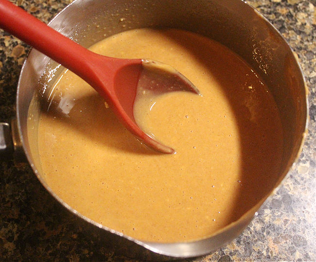 Melted peanut butter in a pan being stirred with a red spoon.