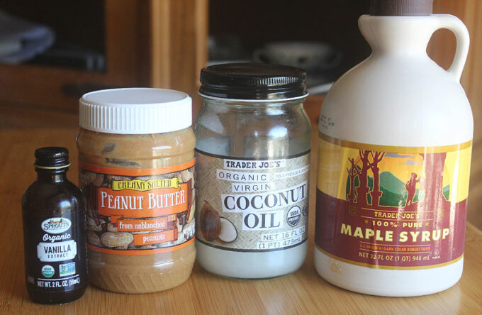 Maple syrup, peanut butter, coconut oil, and vanilla extract on a table.