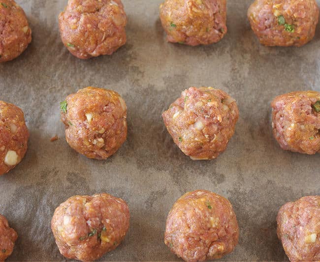 Raw meatballs on a parchment paper-lined baking sheet.