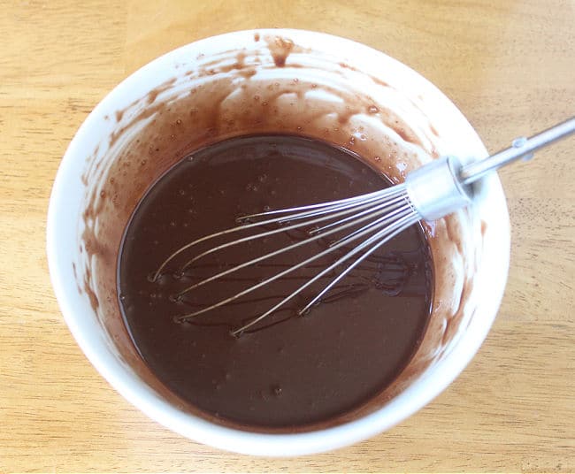 Melted chocolate being whisked in a white bowl.