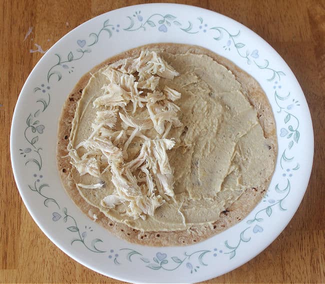 Tortilla with hummus and chicken on a white plate.