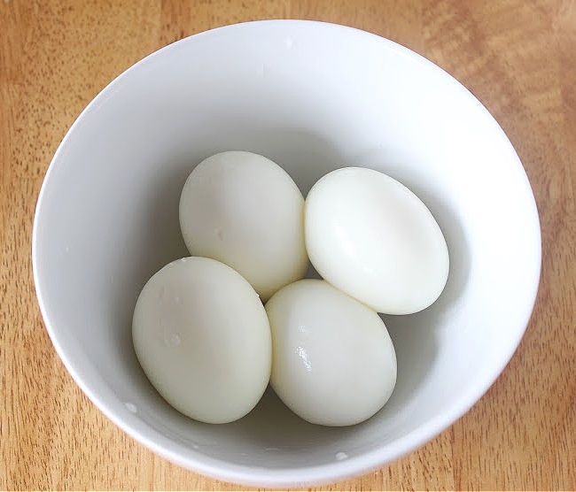 Four hard-boiled eggs in a white bowl.