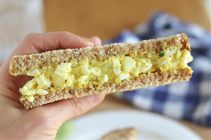 Hand holding half of an egg salad sandwich.