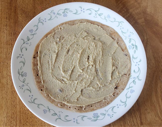 Tortilla with hummus spread on it on a white plate.