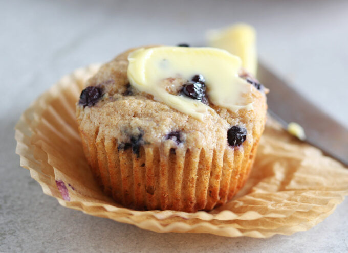 Blueberry muffin topped with butter on a stack of paper muffin cups.