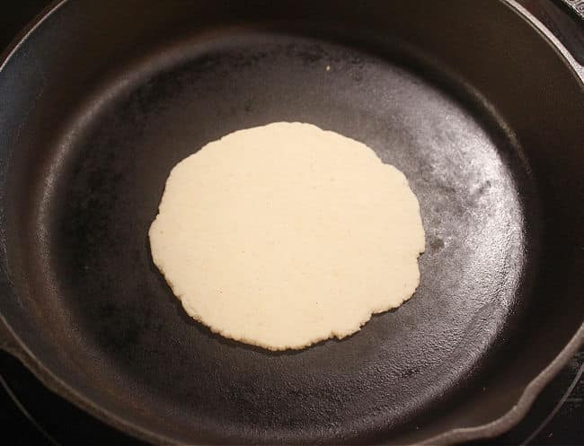 Unbaked corn tortilla in a cast iron skillet.