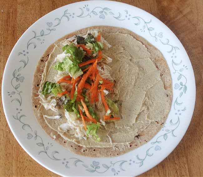 Tortilla with hummus, chicken, and lettuce on a white plate.