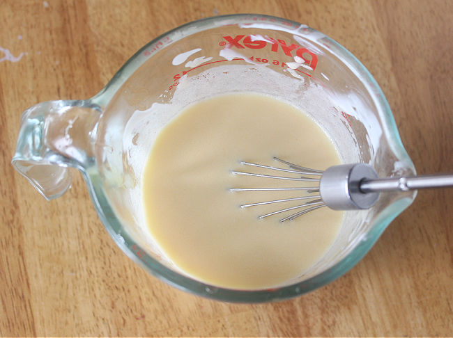 Custard being whisked in a glass pitcher.