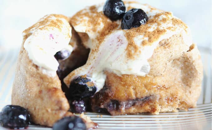 Close-up of the inside of a cinnamon roll with blueberries and cream cheese frosting.