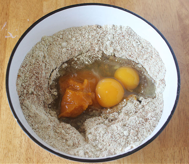 Flour, pumpkin, and eggs in a white bowl.