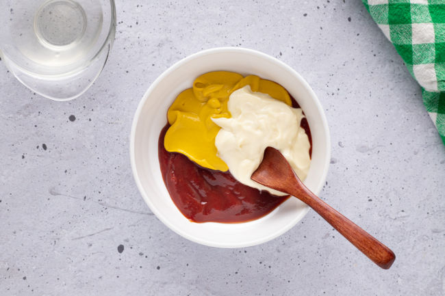 Mixing ketchup, mayo, and mustard in a bowl.