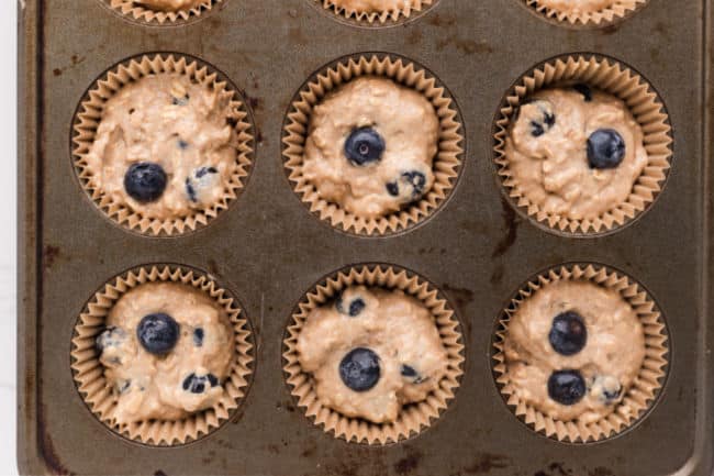 Unbaked blueberry muffin batter in a muffin tin.