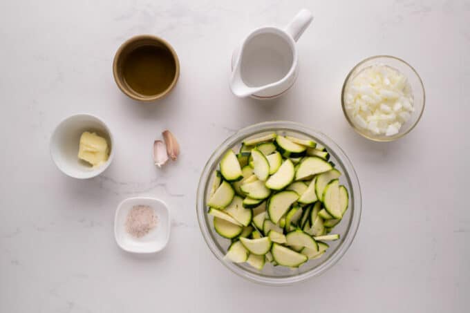 Zucchini, onion, garlic, and olive oil laid out on a table.
