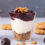 Cheesecake layered in a cup with cookie crumbs and fruit on top.