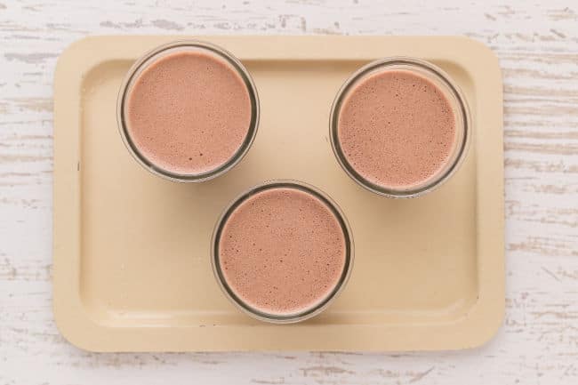 Three cups of chocolate pudding on a tray.