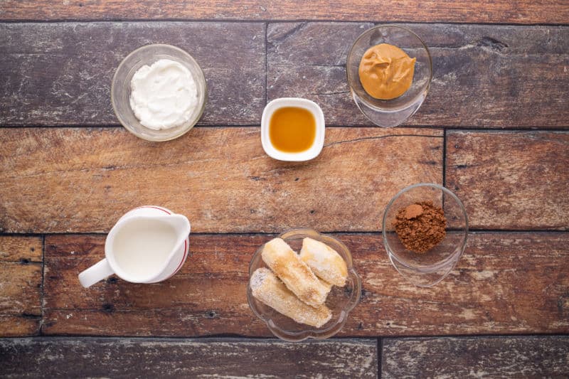 Yogurt, milk, cocoa, and banana laid out on a table.