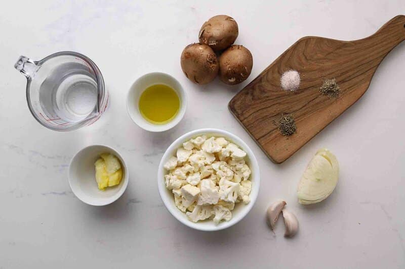 Cauliflower, mushrooms, onion, garlic, and spices laid out on a table.
