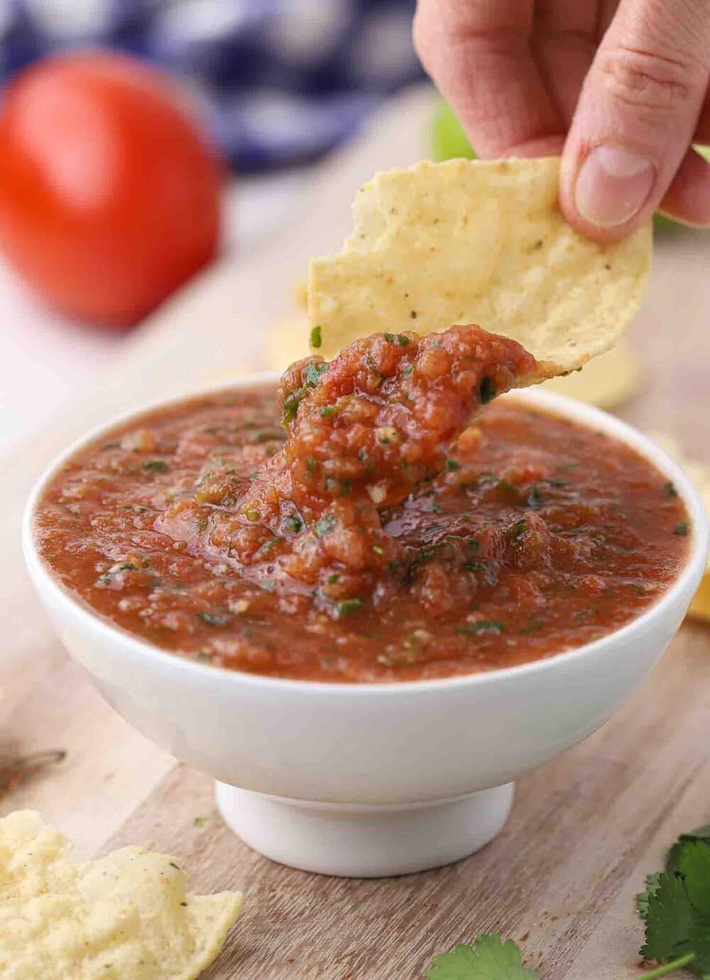 Hand dipping a tortilla chip in salsa.