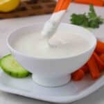 Carrot dipping into a bowl of ranch dressing.